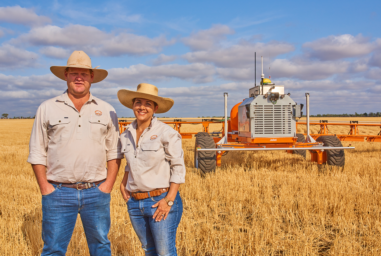 Andrew and Jocie Bate standing in a wheat field beside a SwarmBot